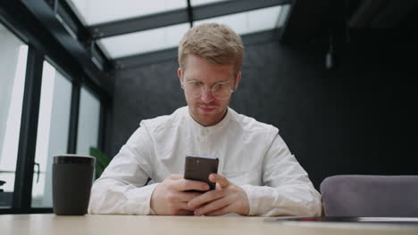 handsome-man-with-glasses-is-using-smartphone-in-cafe-reading-news-in-social-media-frontal-portrait